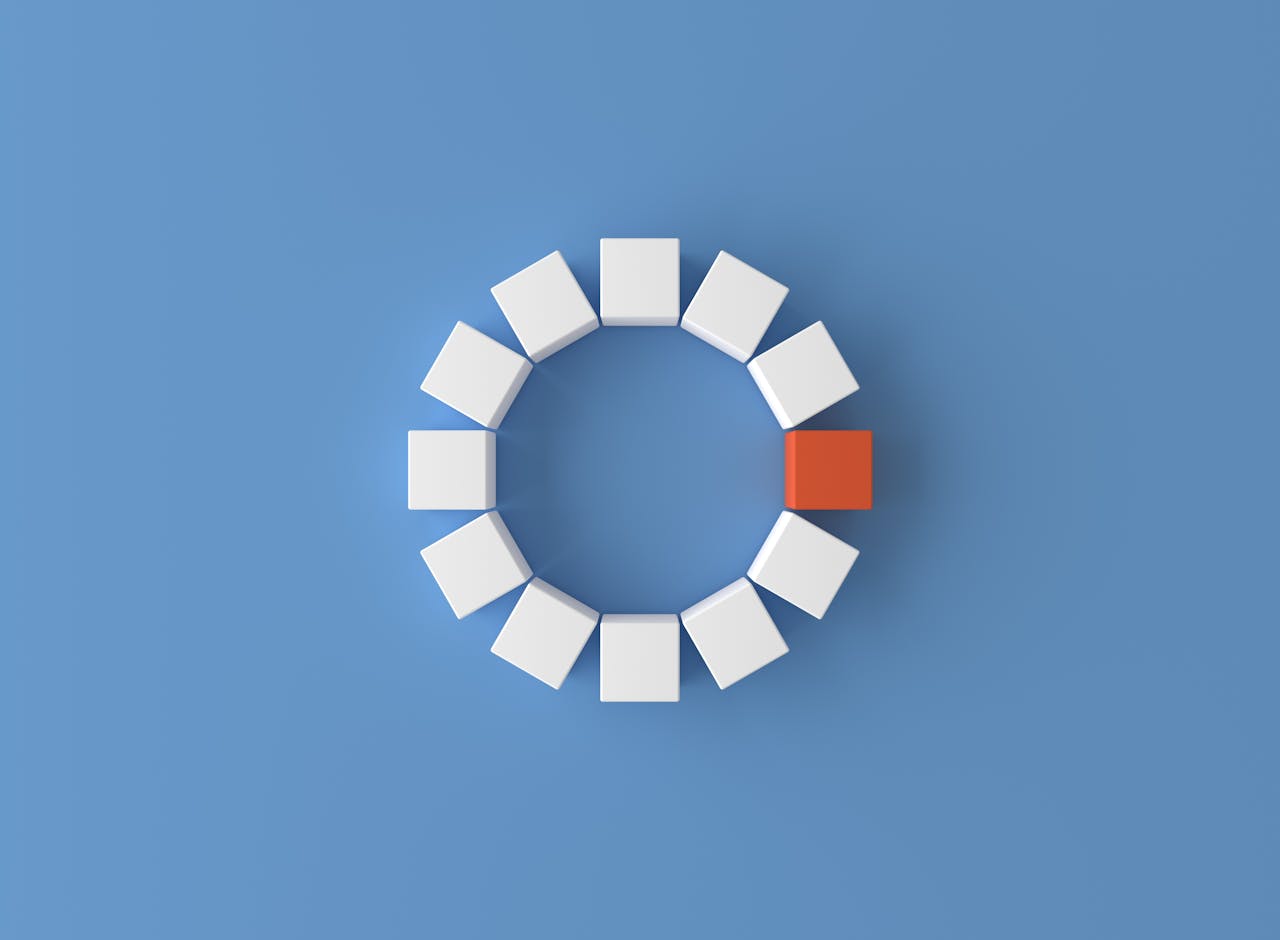 A minimalist 3D render featuring a circle of white cubes with one red cube on a blue background.